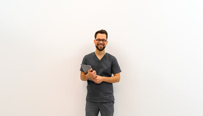 Portrait of confident male doctor holding laptop and smiling at camera while standing against white background