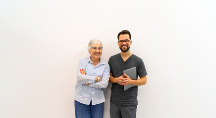 Cheerful senior patient standing with arms crossed beside young doctor and posing confidently over white background