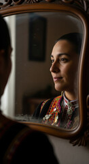 Asian woman in ethnic costume smiling at her reflection in a vintage mirror. Concept of cultural identity, heritage, and beauty.
