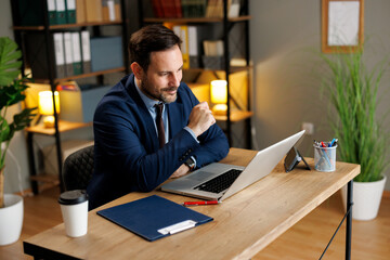 Focused businessman working on laptop at desk in modern office