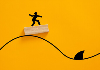 Stick figure surfing on wood block avoiding shark