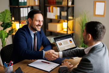 Happy businessmen shaking hands after signing contract in office