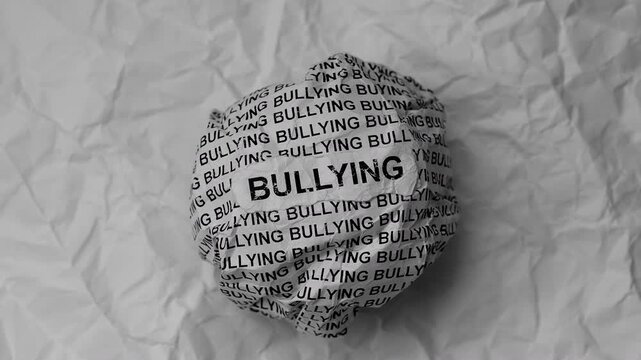 Crumpled paper ball with words Bullying on torn white paper pieces background.