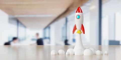 Toy rocket starting on wooden table in front of office background, startup or innovation concept