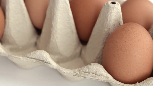 Brown eggs in carton with hand approaching single egg in perspective view showing shell surface and carton divider detail
