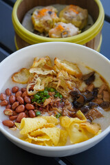 Chicken and mushroom rice porridge with creamy smooth texture, savory toppings, crunchy crackers, peanuts, herbs, and warm comforting flavor, modern Asian breakfast dish with clean appetizing presenta
