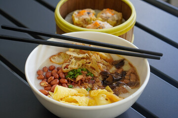 Chicken and mushroom rice porridge with creamy smooth texture, savory toppings, crunchy crackers, peanuts, herbs, and warm comforting flavor, modern Asian breakfast dish with clean appetizing presenta