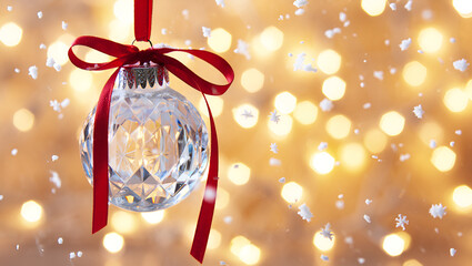 Sparkling crystal christmas ornament with red ribbon against festive golden bokeh lights and falling snow