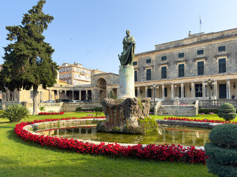 Bronze statue in front of St. Michael and St. George Palace, surrounded by a fountain and red color flowers. Corfu island, Greece.
