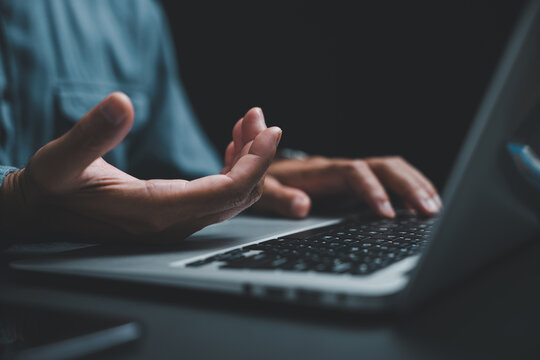 Close-up of hand gesturing over laptop keyboard, dark background. - Powered by Adobe
