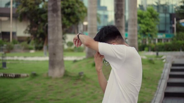 Man jogging in city park, stopping to clean glasses, casual outdoor exercise, urban lifestyle routine, healthy living concept, relaxed morning activity, everyday life motion