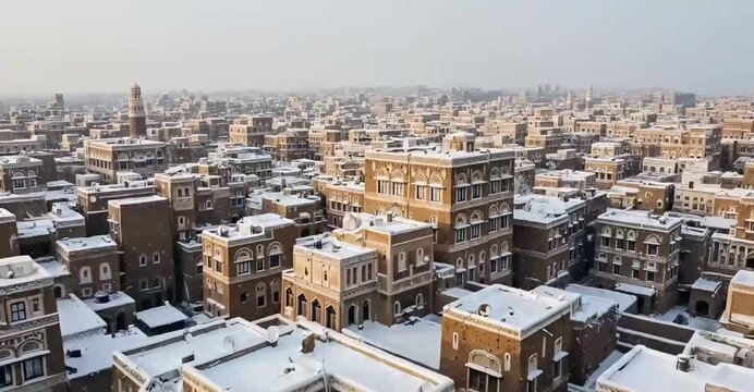 Aerial view of ancient Sana'a city skyscrapers covered in white snow, traditional Yemeni architecture under snowfall, historical heritage buildings in winter.