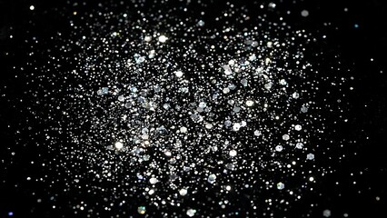 Close-up of sparkling silver glitter scattered on a dark, textured surface, creating a festive and magical abstract background.