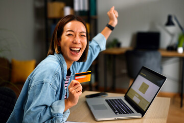 Excited Asian woman celebrating online shopping success with card