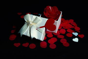 Open and closed gift box with satin ribbon, red and white heart petals on black background for Valentine's Day