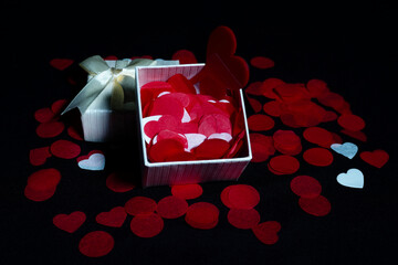 Open and closed gift box with satin ribbon, red and white heart petals on black background for Valentine's Day