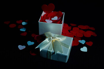 Open and closed gift box with satin ribbon, red and white heart petals on black background for Valentine's Day