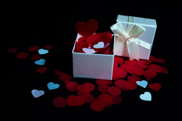 Open and closed gift box with satin ribbon, red and white heart petals on black background for Valentine's Day