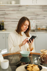 Business woman using smart phone while having breakfast at home