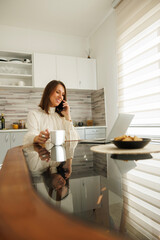 Business woman having phone conversation and working using laptop computer at home
