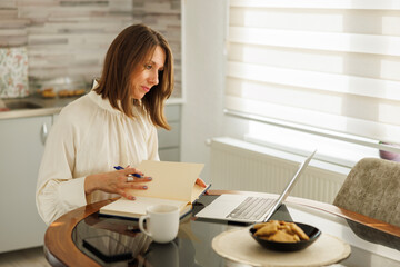 Business woman working remotely from home taking notes while having online meeting