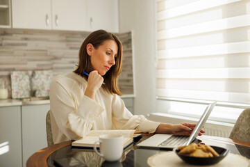 Business woman working remotely from home taking notes while having online meeting