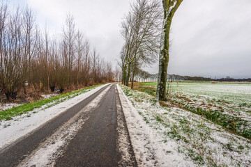 Agricultural landscape in winter. It has just snowed, and car tracks are visible on the country road. The photo was taken on a cloudy day in January.