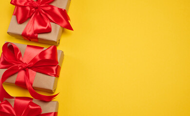 Gift box wrapped in craft paper and tied with a large bright red satin bow on a  yellow background