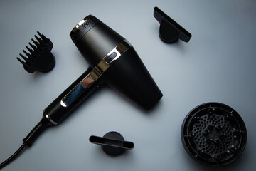 A black hair dryer around which there are different drying attachments - a comb, a diffuser and...