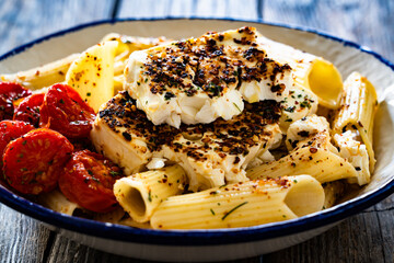 Roasted cherry tomatoes and feta cheese on penne pasta on wooden table	