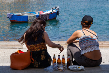 Two women relaxing by the waterfront with beer and snacks