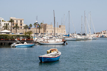 Boats moored in Mediterranean harbor with historic backdrop

