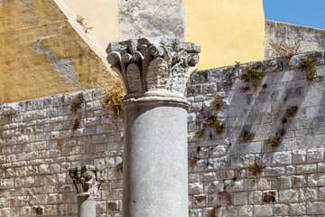 Ancient stone column in front of historic wall and building