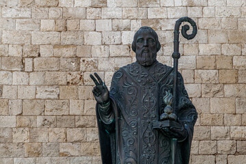 Bronze statue of bishop in front of stone wall
