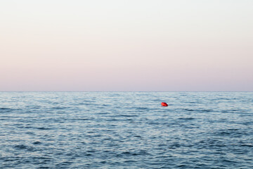 Red buoy floating on calm sea at dusk