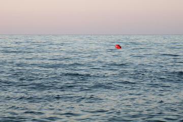 Red buoy floating on calm sea at dusk