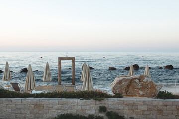 Closed beach umbrellas and stone arch facing calm sea