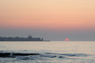 Sunset over calm sea with coastal silhouette