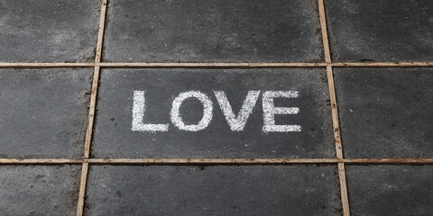 LOVE word written in white chalk on dark concrete tile, construction guideline lines visible, urban outdoor setting, simple and emotional street art