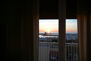 porto di monopoli all'alba visto da una finestra con una tenda