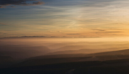 Sunset over layered mountain ranges with mist and a colorful sky.