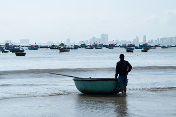 Vietnamese fisherman with traditional baske Vietnames fisherman standing with traditional basket boat on the sea shore.Coastal lifestyle,fishing industry and maritime culture in Vietnam,Southeast Asia
