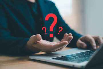 Businessman working on laptop with floating question mark symbol representing problem solving decision making, uncertainty, FAQ, customer support, business strategy and modern technology concept.