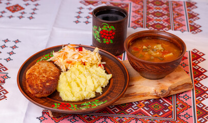 Traditional Ukrainian lunch with mashed potatoes, meat cutlet, vegetable soup and kvass on embroidered tablecloth