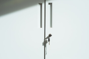 Close-up view of of gray lockable metal storage cabinet door features two vertical cutouts and keyhole with key inserted.