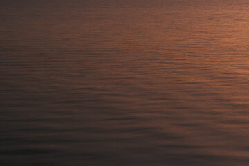 Abstract ocean water surface reflecting warm sunset light with gentle ripples, creating a calm and minimal natural texture suitable for background, luxury design, mindfulness, and atmospheric concepts