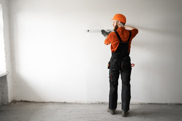 Man builder in hardhat drilling wall with drill perforator. construction or home renovation