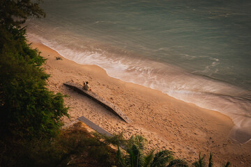 Top-down view of gentle ocean waves washing onto sandy beach with warm sunlight tones, creating a calm natural shoreline texture ideal for background, travel, wellness, and minimal design concepts.