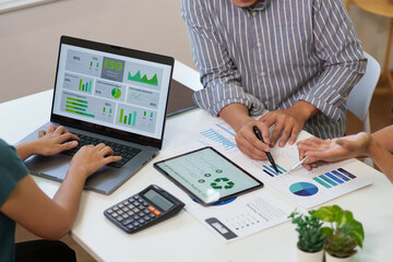 Business professionals analyzing ESG data and sustainable business performance using laptop, tablet, and printed financial charts in a modern office meeting.