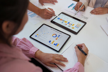 Business colleagues reviewing sale performance charts and financial data on digital tablets during a collaborative team meeting in an office workspace.